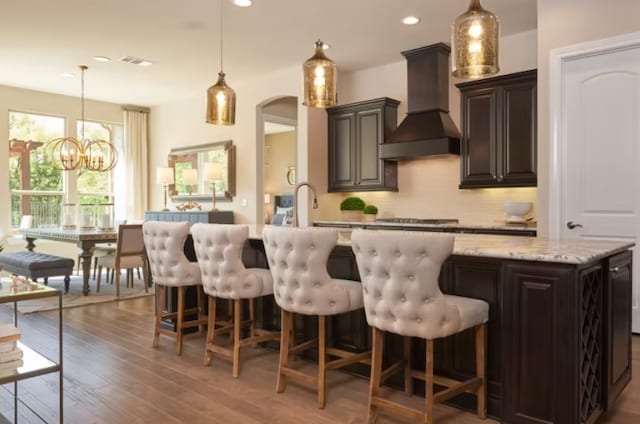 kitchen with dark brown cabinetry, decorative backsplash, hanging light fixtures, and custom range hood