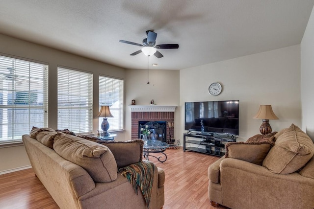 living room featuring a fireplace, ceiling fan, light hardwood / wood-style flooring, and a wealth of natural light