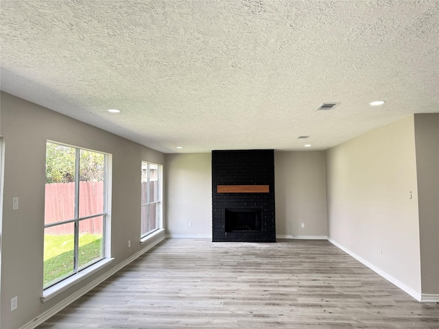 unfurnished living room with a brick fireplace, a textured ceiling, and light wood-type flooring