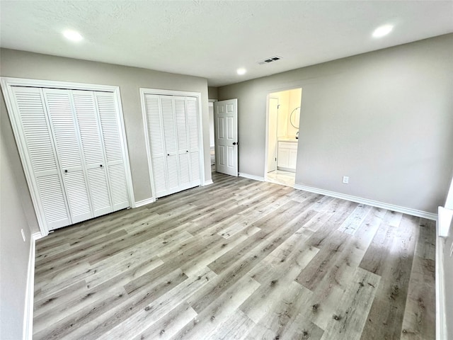 unfurnished bedroom with multiple closets, light wood-type flooring, and ensuite bath