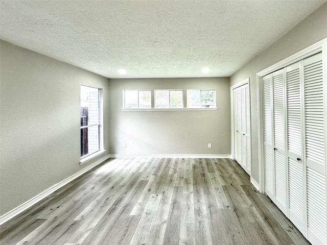 unfurnished bedroom featuring multiple closets, light wood-type flooring, and a textured ceiling