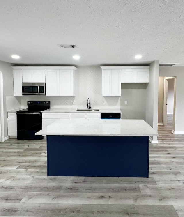 kitchen with sink, black / electric stove, white cabinetry, a textured ceiling, and a kitchen island