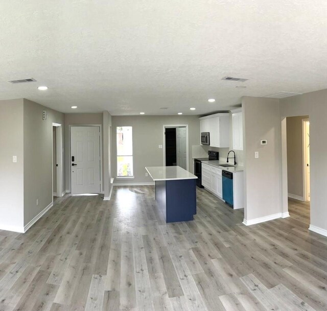 kitchen featuring a textured ceiling, white cabinets, a center island, black / electric stove, and sink