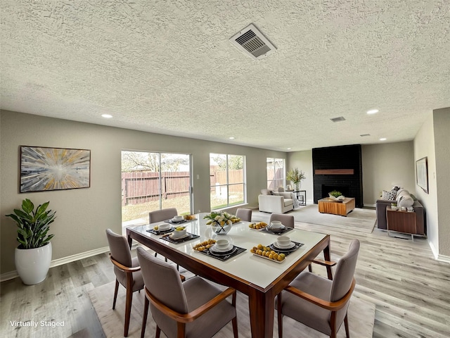 dining space with light hardwood / wood-style floors, a textured ceiling, and a fireplace