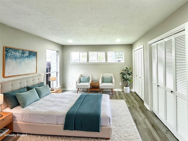 bedroom with two closets, wood-type flooring, multiple windows, and a textured ceiling