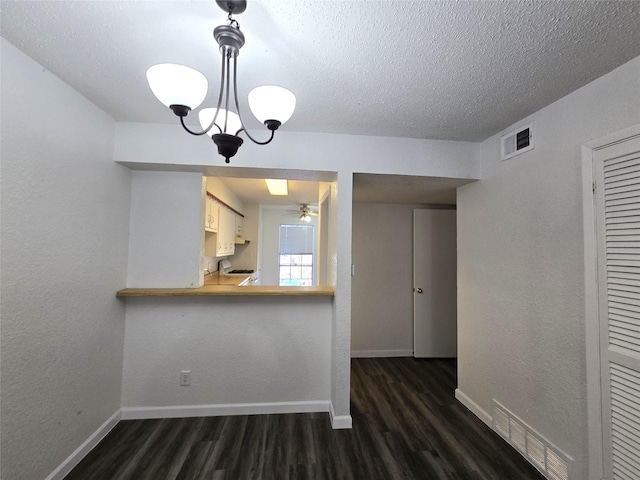 kitchen featuring kitchen peninsula, dark hardwood / wood-style floors, decorative light fixtures, a textured ceiling, and ceiling fan with notable chandelier