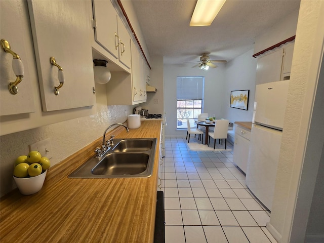 kitchen with sink, white cabinetry, light tile patterned floors, and white fridge