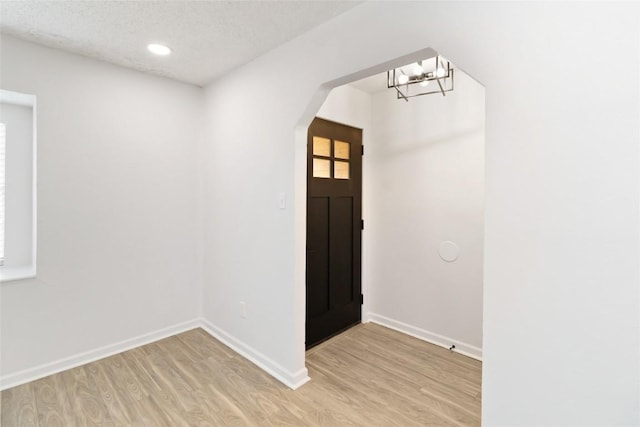 entryway with a textured ceiling, light wood-type flooring, and an inviting chandelier