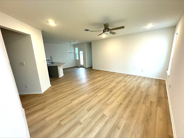 unfurnished living room with sink, ceiling fan with notable chandelier, and light hardwood / wood-style floors