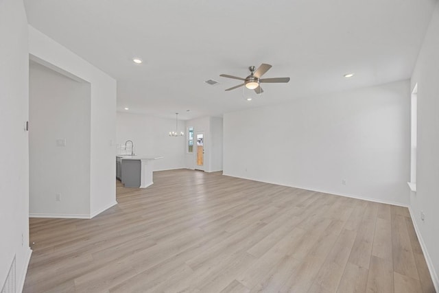 unfurnished living room with light wood finished floors, visible vents, a sink, and ceiling fan with notable chandelier