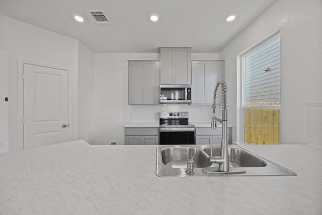 kitchen featuring visible vents, light countertops, stainless steel appliances, gray cabinetry, and a sink