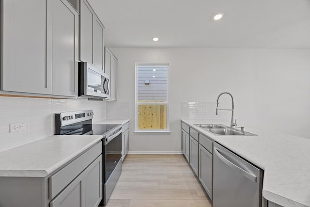 kitchen featuring stainless steel appliances, a sink, light countertops, gray cabinets, and tasteful backsplash