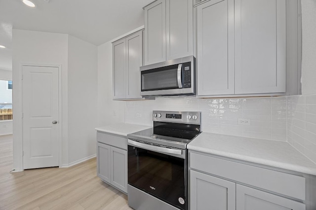 kitchen with light wood finished floors, light countertops, appliances with stainless steel finishes, and tasteful backsplash