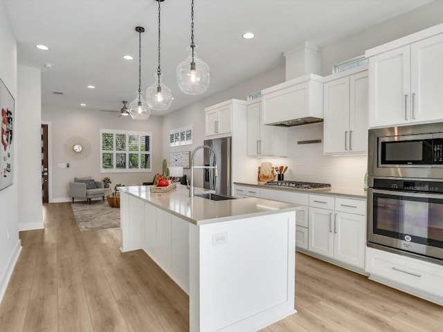 kitchen with hanging light fixtures, sink, an island with sink, appliances with stainless steel finishes, and white cabinetry