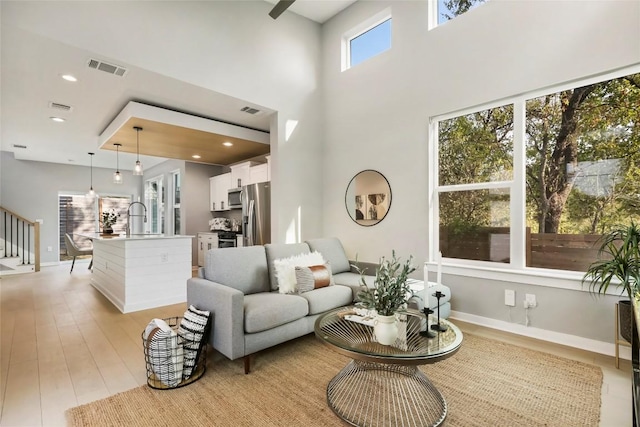 living room with a towering ceiling, sink, and light hardwood / wood-style flooring