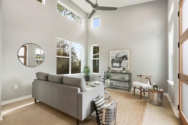 living room featuring a towering ceiling, light hardwood / wood-style floors, and ceiling fan