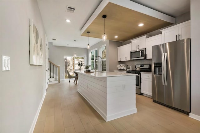 kitchen with sink, stainless steel appliances, decorative light fixtures, a kitchen island with sink, and white cabinets