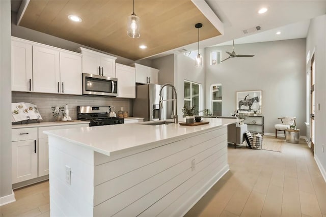 kitchen featuring appliances with stainless steel finishes, white cabinetry, a kitchen island with sink, and sink