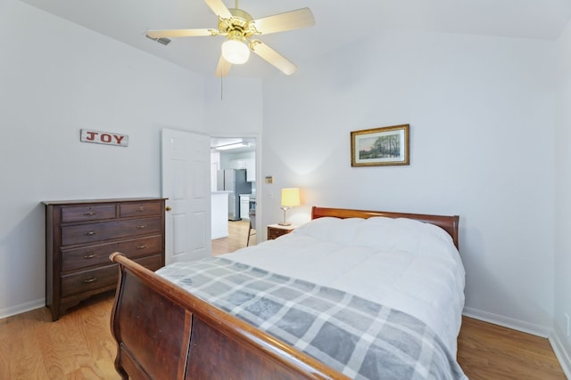 bedroom with ceiling fan, stainless steel fridge, vaulted ceiling, and light hardwood / wood-style flooring