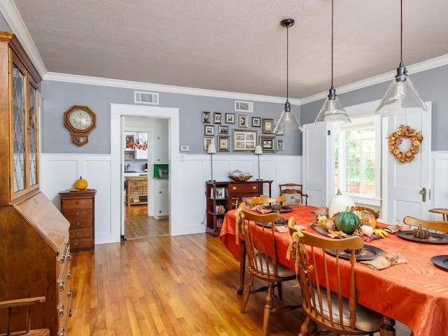 dining area featuring a textured ceiling, light hardwood / wood-style floors, and crown molding