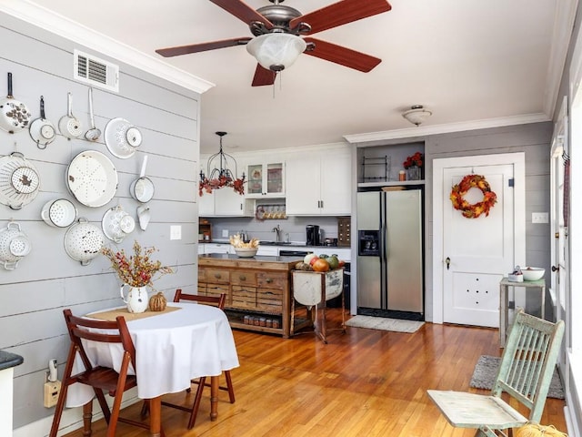 kitchen featuring stainless steel refrigerator with ice dispenser, light wood-type flooring, ornamental molding, decorative light fixtures, and white cabinetry