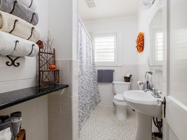 bathroom with tile patterned flooring, toilet, tile walls, and a wealth of natural light