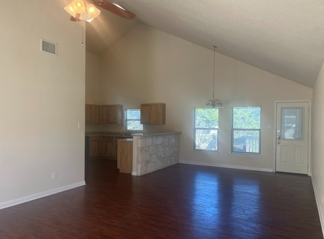 unfurnished living room featuring a wealth of natural light, high vaulted ceiling, dark wood-type flooring, and ceiling fan with notable chandelier