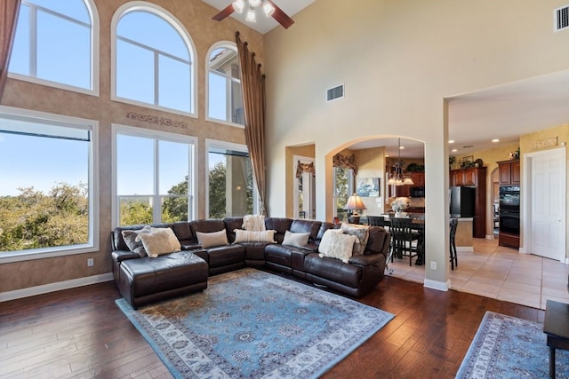 living room with dark hardwood / wood-style flooring, a towering ceiling, and ceiling fan with notable chandelier