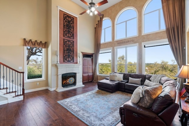 living room with a high ceiling, dark hardwood / wood-style flooring, ceiling fan, and a healthy amount of sunlight