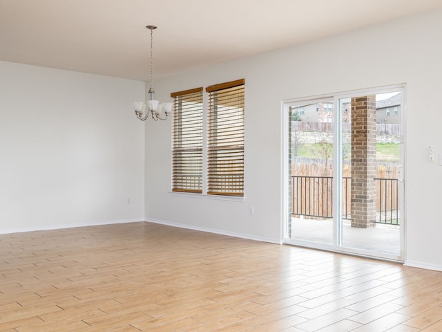 spare room with a chandelier and light wood-type flooring