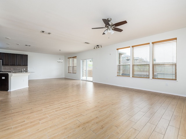 unfurnished living room with ceiling fan with notable chandelier and light hardwood / wood-style floors