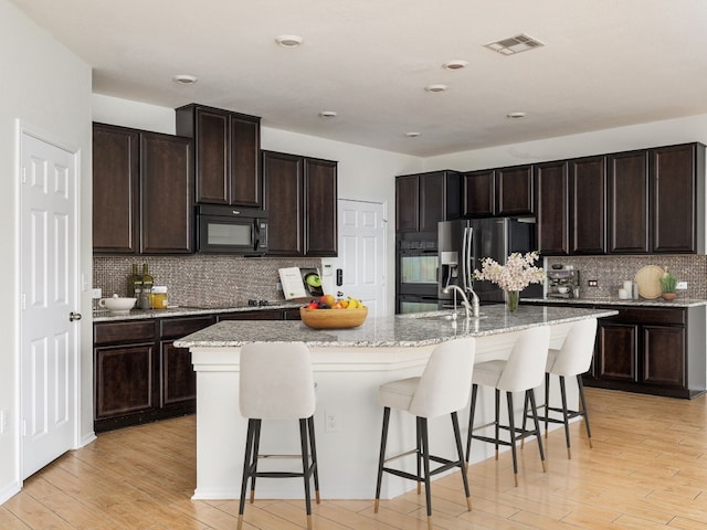 kitchen featuring black appliances, a kitchen breakfast bar, dark brown cabinets, and a kitchen island with sink