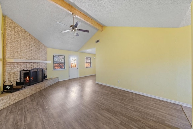 unfurnished living room featuring ceiling fan, vaulted ceiling with beams, a textured ceiling, a fireplace, and hardwood / wood-style flooring