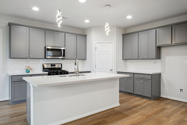 kitchen featuring gray cabinetry, pendant lighting, sink, an island with sink, and appliances with stainless steel finishes