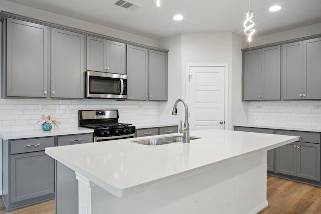 kitchen featuring gray cabinetry, sink, light hardwood / wood-style flooring, an island with sink, and stainless steel appliances