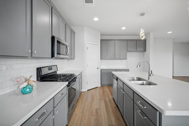 kitchen with appliances with stainless steel finishes, sink, gray cabinets, and an island with sink