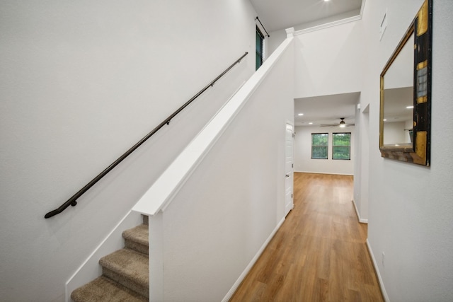 stairway with ceiling fan, a towering ceiling, and wood-type flooring