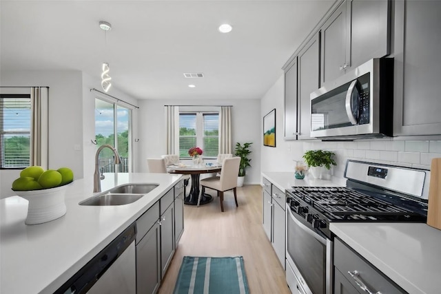 kitchen featuring decorative backsplash, appliances with stainless steel finishes, gray cabinetry, sink, and hanging light fixtures