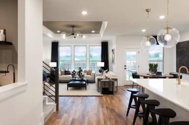 kitchen featuring a breakfast bar area, a healthy amount of sunlight, hardwood / wood-style floors, decorative light fixtures, and a tray ceiling