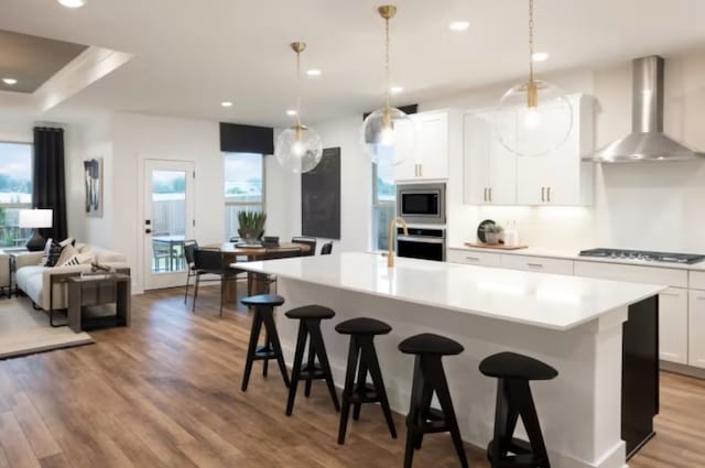 kitchen featuring white cabinetry, wall chimney range hood, a spacious island, decorative light fixtures, and appliances with stainless steel finishes