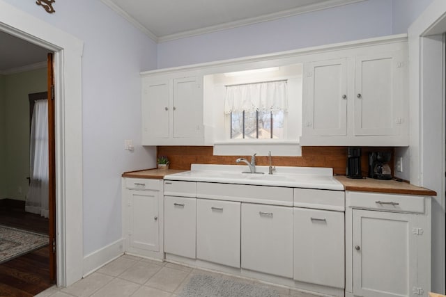 kitchen featuring white cabinets, light tile patterned flooring, ornamental molding, and sink