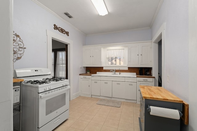 kitchen with decorative backsplash, crown molding, white cabinets, white gas stove, and light tile patterned flooring