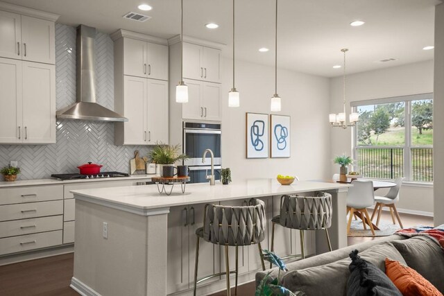 kitchen featuring appliances with stainless steel finishes, a kitchen breakfast bar, wall chimney range hood, hanging light fixtures, and an island with sink