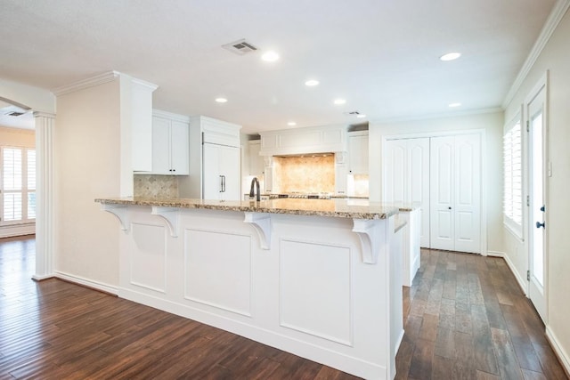 30102 Carmel Bay St, Georgetown, TX 78628 - kitchen featuring backsplash, a peninsula, light stone counters, dark wood-style flooring, and ornamental molding