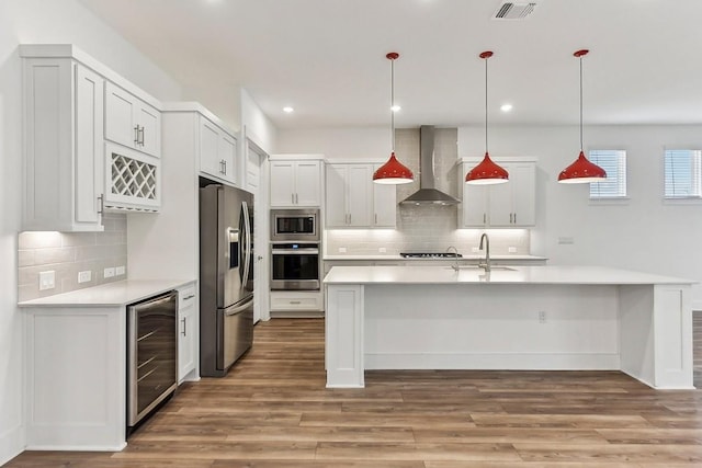 kitchen featuring stainless steel appliances, beverage cooler, wall chimney range hood, white cabinetry, and hanging light fixtures