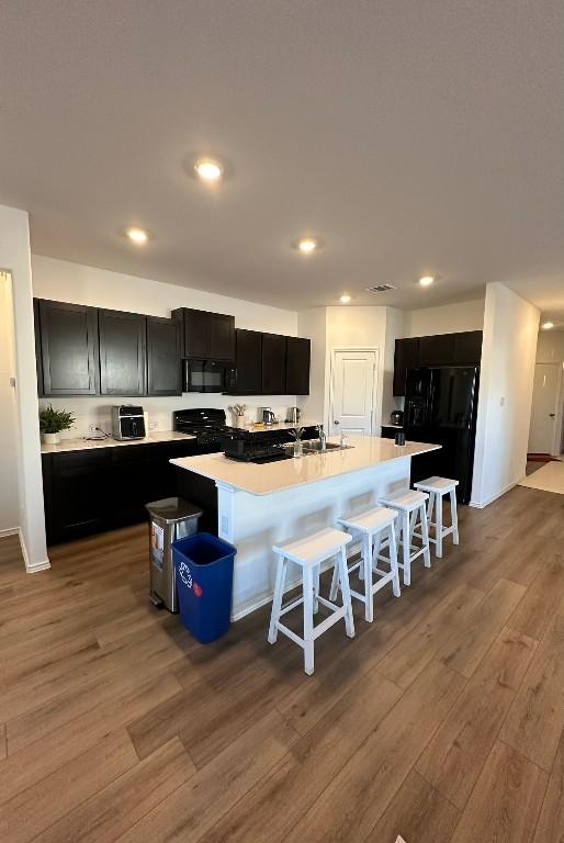 kitchen featuring a breakfast bar, light wood-type flooring, a kitchen island with sink, and black appliances