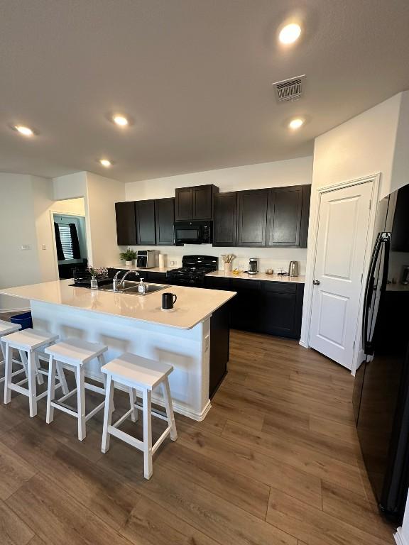 kitchen with black appliances, sink, dark hardwood / wood-style floors, an island with sink, and a breakfast bar area