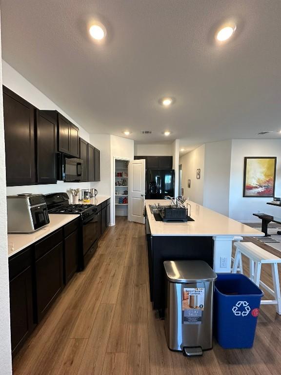 kitchen with sink, black range with gas cooktop, an island with sink, fridge, and light wood-type flooring