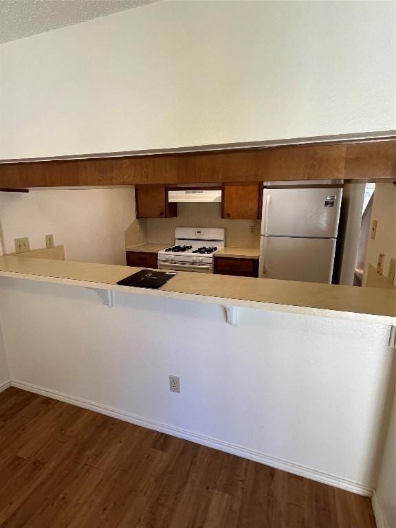 kitchen with kitchen peninsula, white appliances, a breakfast bar area, and dark hardwood / wood-style flooring