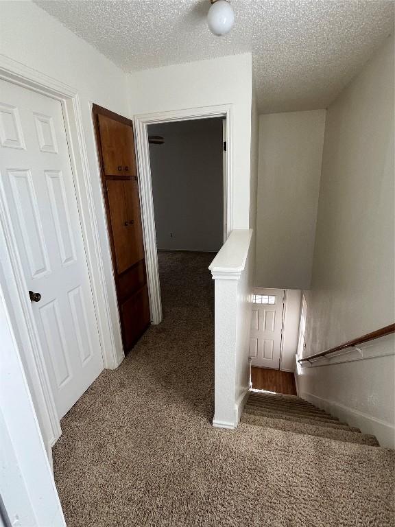 hall with dark colored carpet and a textured ceiling